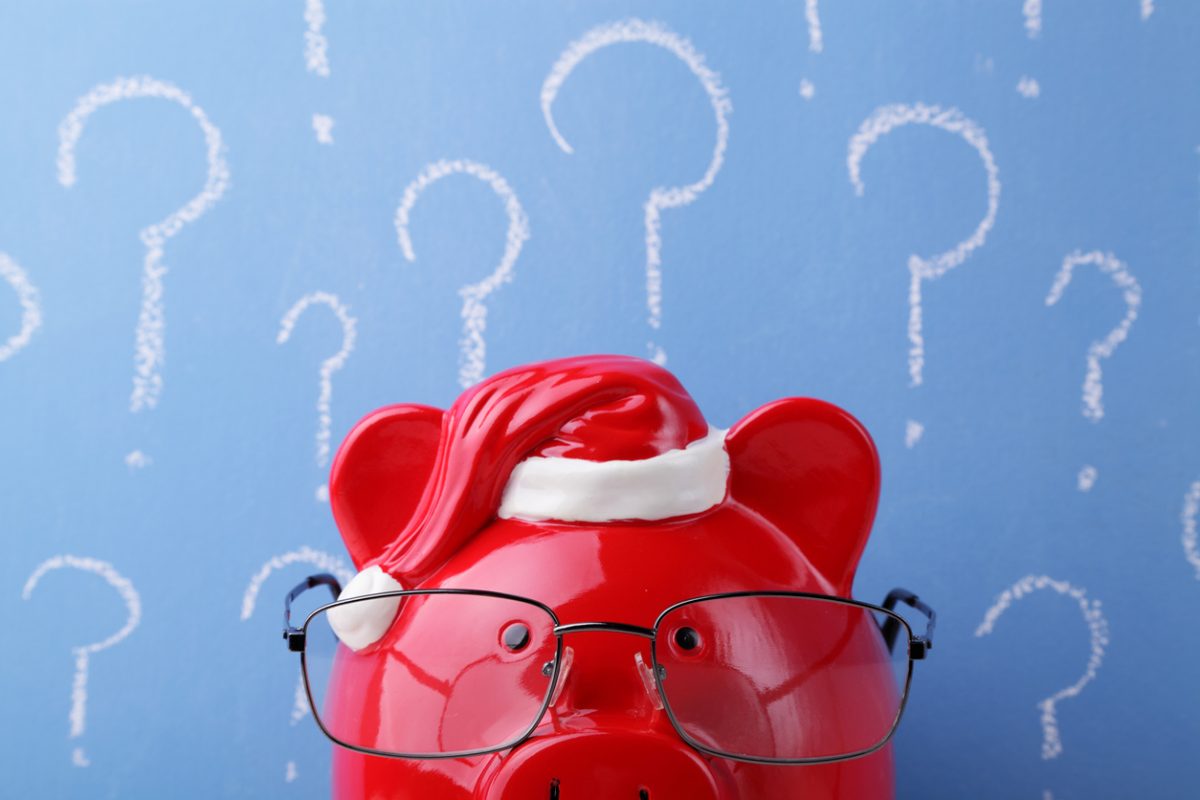 Piggy bank wearing santa hat against background of question marks