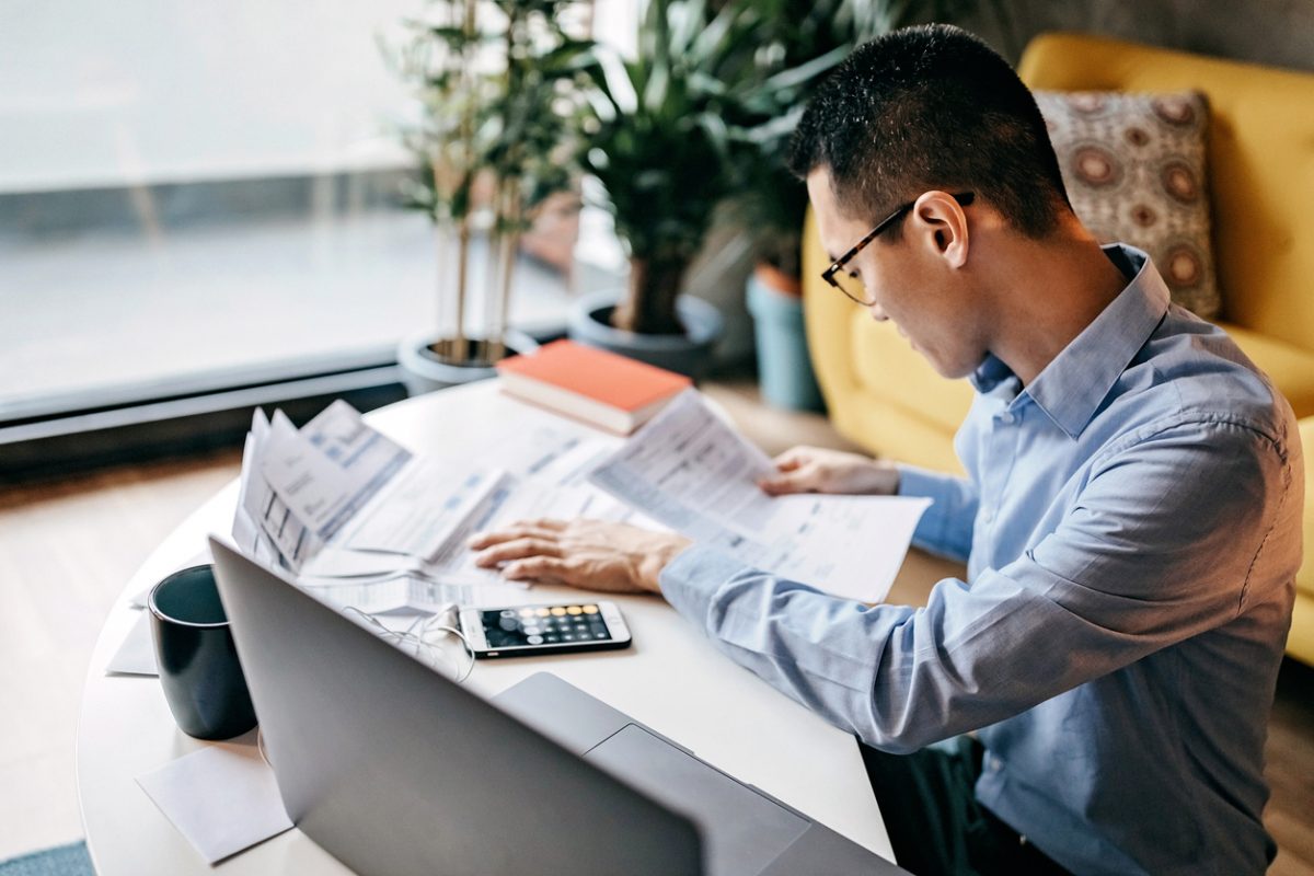 Man calculating finances with laptop and paperwork